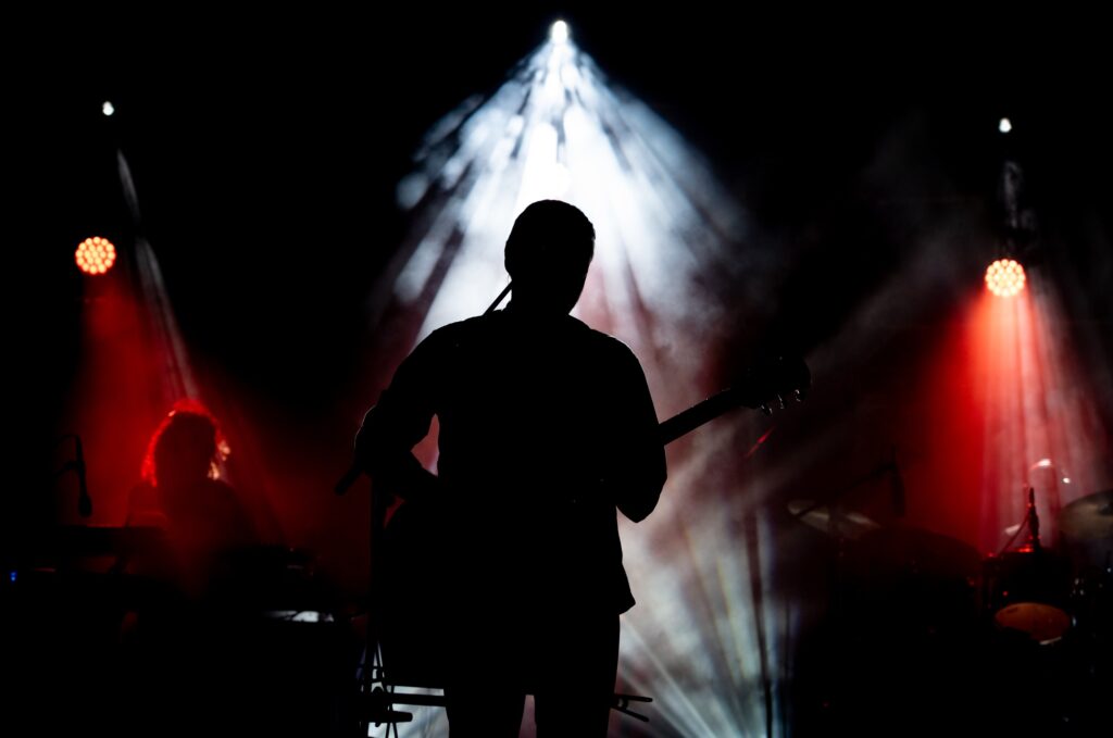 Musician playing guitar performing on stage under spot light. Silhouette of a music artist and band